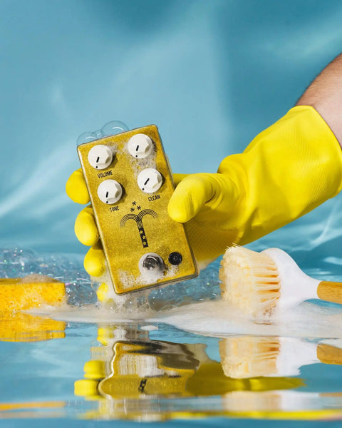 Person holds Morning Glory Clean Overdrive Pedal With Transparent Tone, Clear Pick Attack in yellow glove above reflective surface.
