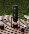 Proven Travel Espresso Stand And Universal Coffee Maker Rack With No Sweat Assembly For Drip Brewers And Portable Grinder Kits That Keeps Your Morning Brew Routine Fully Locked In on wooden table with grass background.