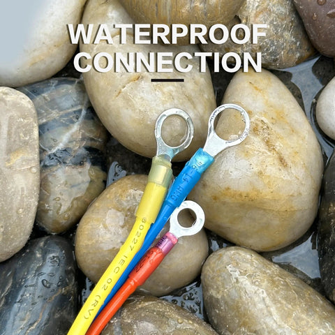 Heat-shrink wire terminals; three insulated ring terminals in yellow, blue, and orange on wet pebbles.