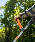 Close-up of a hand gripping the handle of a 20V Cordless Garden Tiller Cultivator with 7.5 Inch Width, set against greenery.
