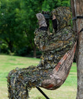 Person seated in Camo Tree Hammock Chair Portable Hunting Stool For Outdoors attached to a tree in a camouflage outfit, using binoculars.