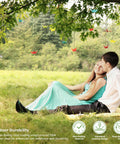 Couple sitting under trees with hanging decorations, showcasing the outdoor use of Black Vinyl Coated Wire Rope One Sixteenth Inch 328 Feet Stainless Steel Cable With 150 Aluminum Crimp Sleeves For String Lights Clotheslines Trellis And Picture Hanging Easy Install.