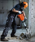 Worker using Beast 2200W Electric Demolition Jack Hammer Kit With 1400 BPM for concrete removal, wearing safety gear.