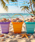 Three Pack Collapsible Beach Buckets For Kids And Toddlers, Foldable Sand Toys in Purple, Blue, Yellow on a sandy beach with shells