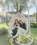 Two people sitting in Hanging Egg Chair Outdoor Indoor With Stand, Wicker Swing Egg Chair in a garden, white, PE rattan weave.