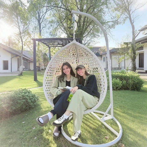 Two people sitting in Hanging Egg Chair Outdoor Indoor With Stand, Wicker Swing Egg Chair in a garden, white, PE rattan weave.