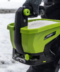 Person using 20-Volt Cordless Handheld Seed And Fertilizer Spreader For Yard Work With Adjustable Spreading Rate Dial on snow