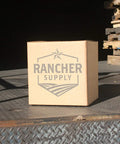 Cardboard box labeled 'Rancher Supply' on a metal platform near stacked pallets in a warehouse