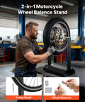Man using motorcycle wheel balancer and truing stand with adjustable centering cones and truing pointer in workshop.