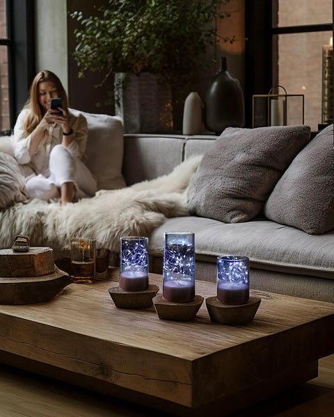Set Of 3 Flameless Candles In Gray Glass Cylinders With Remote For A Cozy Vibe arranged on a wooden table in a living room