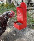 Heavy Duty Metal Chicken Oyster Shell And Grit Feeder With Smart Auto Dispenser, red grit feeder, served to hen, set up on a wire fence.