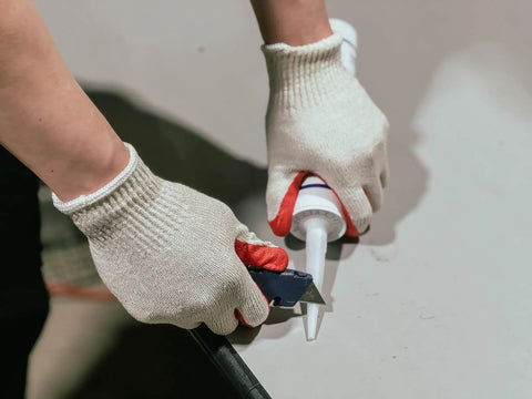 Person using caulking gun while wearing Red Work Gloves Pack Of 300 Touch Screen Ready Latex Palm Coated Nitrile Safety Gloves
