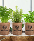All In One Kitchen Windowsill Herb Garden Starter Kit That Makes Growing Basil Parsley Rosemary Thyme Mint A Breeze With Five Seed Varieties Planter Box Bags Discs Markers Tools Pruner Water Bottle And Easy DIY Guide, showing three burlap planter bags with herbs.