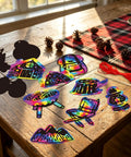Camping Scratch Card Kit 24 Pack For Outdoor Parties displaying 12 unique rainbow designs with wooden sticks and red string on a table.