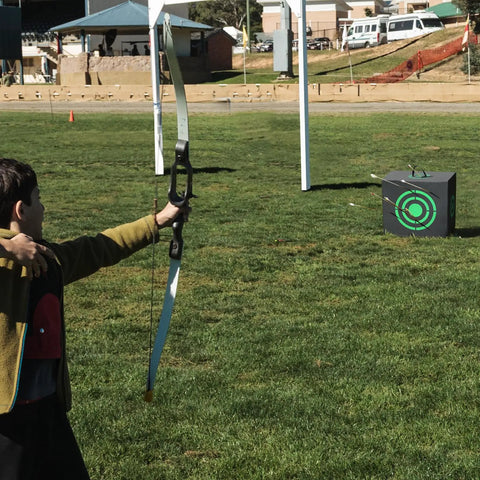Child aiming at All-Side 16x18 Archery Target Block for Outdoor Practice on grass field, clear view of target with arrows, Black