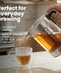 Electric Tea Kettle With Infuser For Loose Leaf Tea No Plastic Touching Water Temperature Control Automatic Shut Off 1.5L Borosilicate Glass Hot Tea Maker pouring tea into cup on kitchen counter.