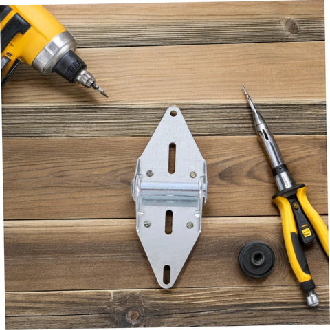 Metal garage door hinge with wheel roller and mounting plate on wood, drill and utility knife nearby.