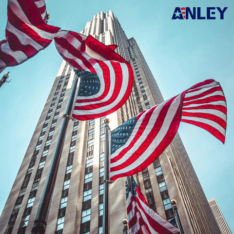 American flags waving on flagpoles in front of a skyscraper, showcasing urban architecture and patriotism.