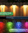 4 Pack Solar Outdoor Lights With RGB Color Changing And Warm White Modes illuminating a fence and wall in yard.