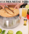 Large Double Wall Stainless Steel Ice Bucket With Lid And Tongs Bpa Free Drink Cooler with ice and cocktails on a table.