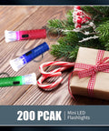 Bulk Pack Of 100 Mini LED Flashlight Keychains In Assorted Colors with candy canes and gift on a wooden surface