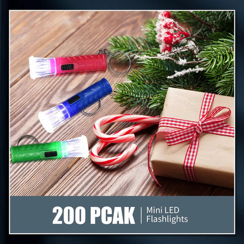 Bulk Pack Of 100 Mini LED Flashlight Keychains In Assorted Colors with candy canes and gift on a wooden surface
