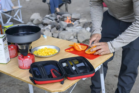 Man using Alpine Deluxe Outdoor Kitchen Set With Zippered Carry Case BPA Free Tools by a campfire, showing folding utensil set.