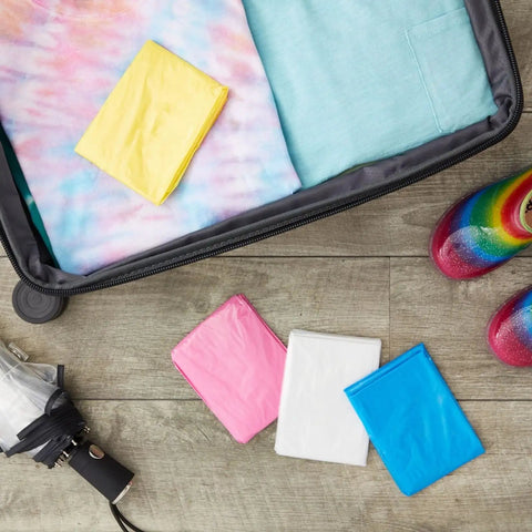 Kids Rain Ponchos Pack Of 20 Disposable With Hood, 4 assorted colors folded next to packed clothes and rain boots, 42 x 60 inches.