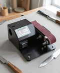 Compact Mini Electric Belt Sander With A Kickass Motor For Handheld Wood Sanding And Fast Metal Polishing Quick Rust Removal And Smooth DIY Finishes Built Like A Rock Solid Workhorse on workbench with knife