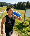 Man drinking from a 500ml flask wearing High Visibility Reflective Running Vest Hydration Backpack Plus 500ml Soft Flask on trail
