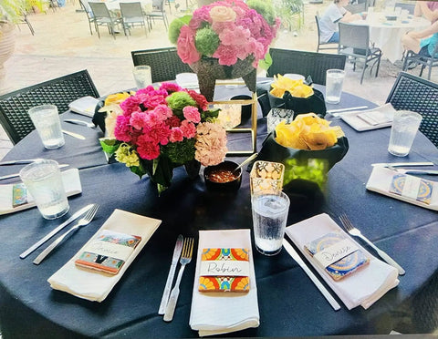 Restaurant table setting with Mexican Tile Mix 100 Tiles 4x4 Ceramic Squares as napkin holders, surrounded by floral centerpieces.