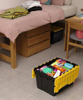 Heavy Duty 12 Gallon Storage Containers With Attached Lids, Stackable Workshop Totes For Garage Organization Setup, Built Like A Tank Plastic Bins In Black And Yellow filled with various items next to a bed.