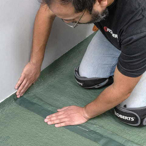 Person applying Easy Peel Overlap Tape on Top Shelf Premium Underlayment One Hundred Square Foot Roll for flooring.