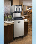 No Drama Countertop Nugget Ice Maker And Water Dispenser with stainless steel finish and push controls, set in a modern lobby.