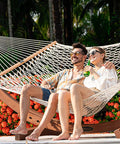 Two people relaxing on a 12 Ft Double Rope Hammock With 13 Ft Brown Wooden Arc Stand For Outdoor Patio And Poolside Chill Session.