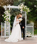 White PVC Garden Arch With Gate For Weddings And Outdoor Decor with flowers and couple standing beneath in an outdoor setting.