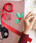 Fabric scissors with black handles and stainless blades beside red ribbon on gift-wrapping setup