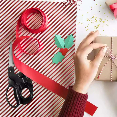 Fabric scissors with black handles and stainless blades beside red ribbon on gift-wrapping setup