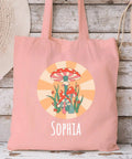 Canvas tote bag with mushroom design and 'Sophia' text, displayed against a rustic wooden wall with straw hats.