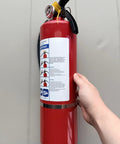 Four Pack Five Lb Abc Dry Chemical Fire Extinguisher Set Featuring No Fuss Quick Release Pin, red steel unit held in hand.