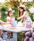 Children at a party with Tie Dye Party Favor Bags With 36 Stickers 30 Pack Mermaid Unicorn Themed Goodie Bags on a table.