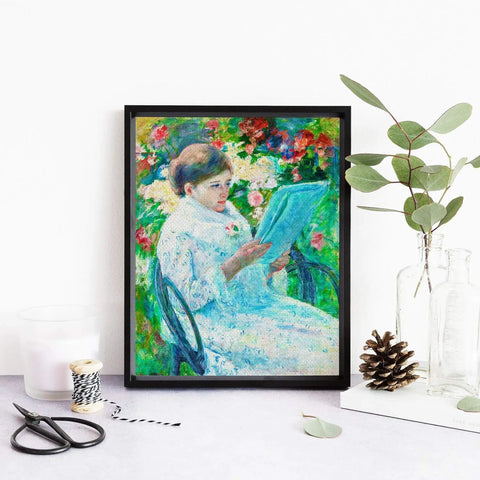 Framed art print of a woman in a garden reading, displayed on a table with decorative items, like pine cones and leaves.