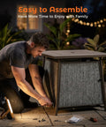 Man assembling 50,000 BTU Propane Fire Pit Table, 28 Inch Square, 2 In 1 Outdoor Fire Pit with Lid, on patio at night.
