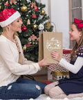 Mother and daughter exchanging 100 Pack Kraft Paper Gift Bags With Handles, Medium Brown, Christmas scene, tree in background.
