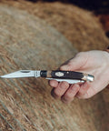 Solid As A Rock Pocket Folder With 2 Inch Clip Point Blade Crafted From High Carbon Stainless Steel And Rough Cut Sawcut Grip held, outdoors.