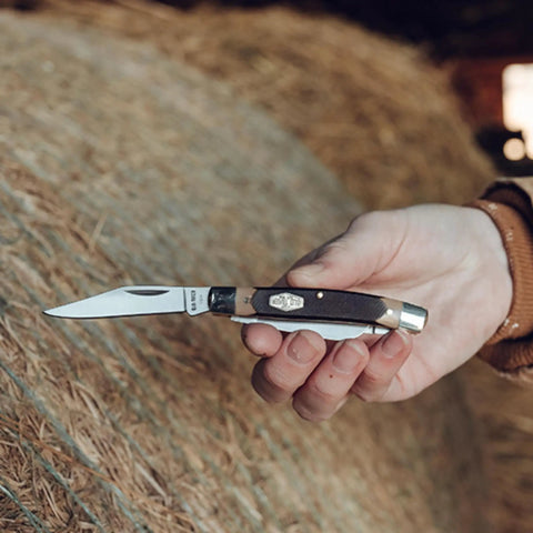 Solid As A Rock Pocket Folder With 2 Inch Clip Point Blade Crafted From High Carbon Stainless Steel And Rough Cut Sawcut Grip held, outdoors.