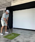 Golfer using Complete Golf Practice Backdrop Enclosure Gear With Poles Corner Connectors Side And Top Netting Impact Screen And Carry Bag For A 10 Feet By 8 Feet Indoor Home Golf Setup in a warehouse setting