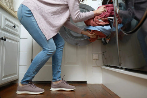 Person loading laundry into machine, highlighting Smart WiFi Water Leak Detector With Real Time Text And Email Alerts, no hub needed