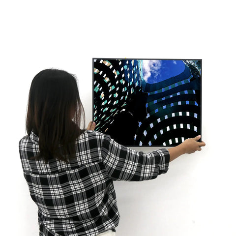 Person hanging a framed picture using Badass Heavy Duty Picture Hangers With Tough Aluminum Grip on a white wall.