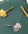 Gold and silver leaf-shaped chopstick rests on dark green surface, showcasing elegant modern tableware design